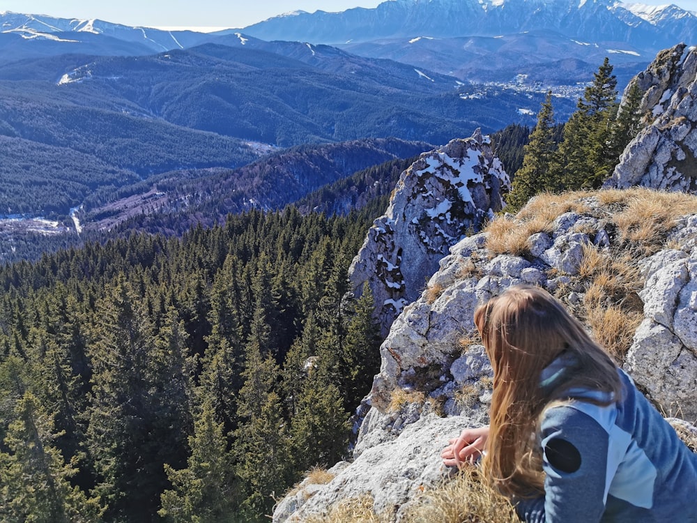 woman in white jacket sitting on rock mountain during daytime