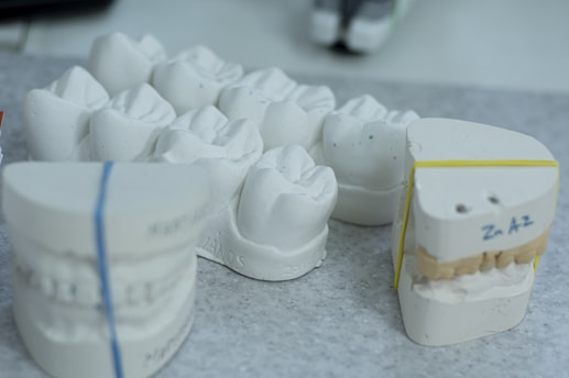 Plaster dental molds are arranged on a gray speckled surface. Some molds are stacked and secured with rubber bands, displaying detailed impressions of teeth.