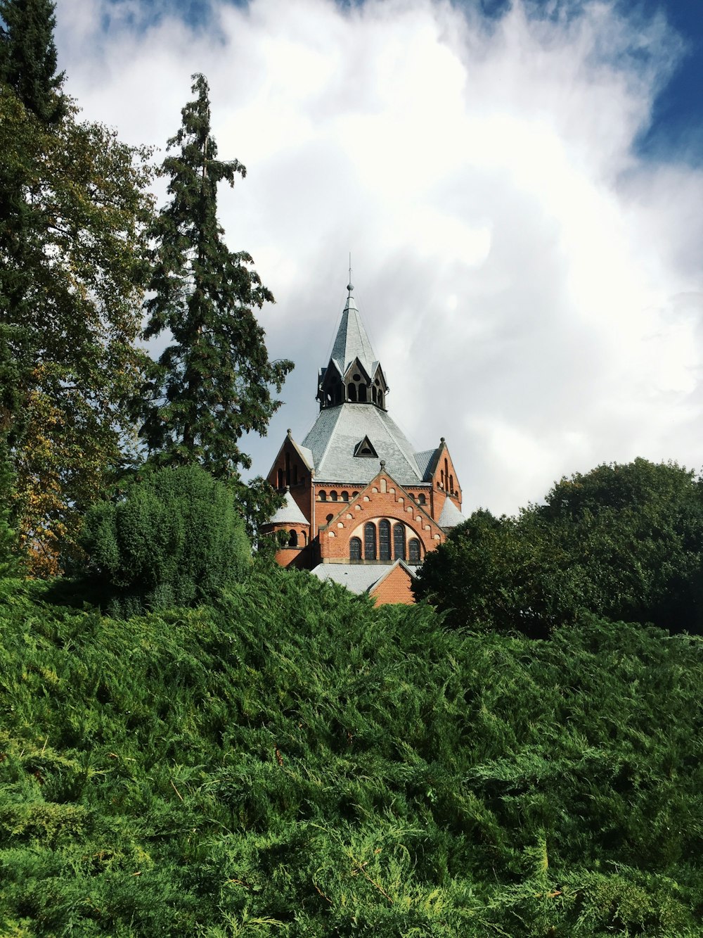 brown and black concrete building surrounded by green trees under white clouds during daytime