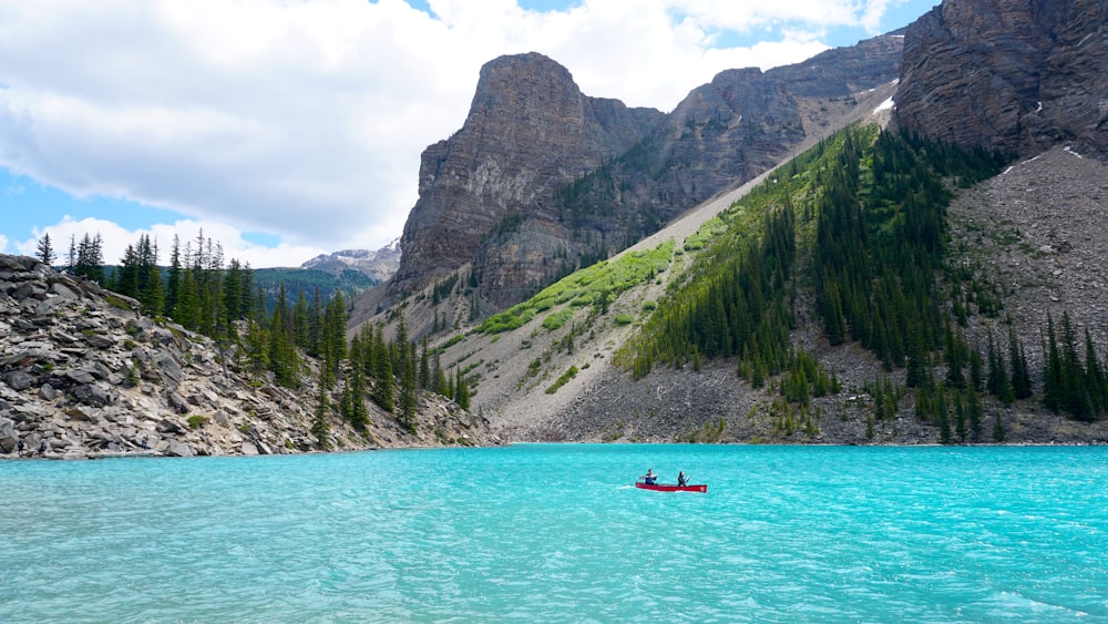 person riding on red kayak on blue sea near green mountain during daytime