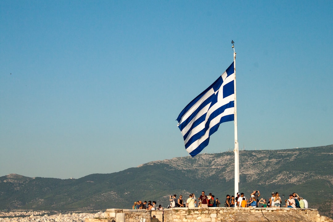 a group of people standing next to a flag, Greek flag on the Acropolis