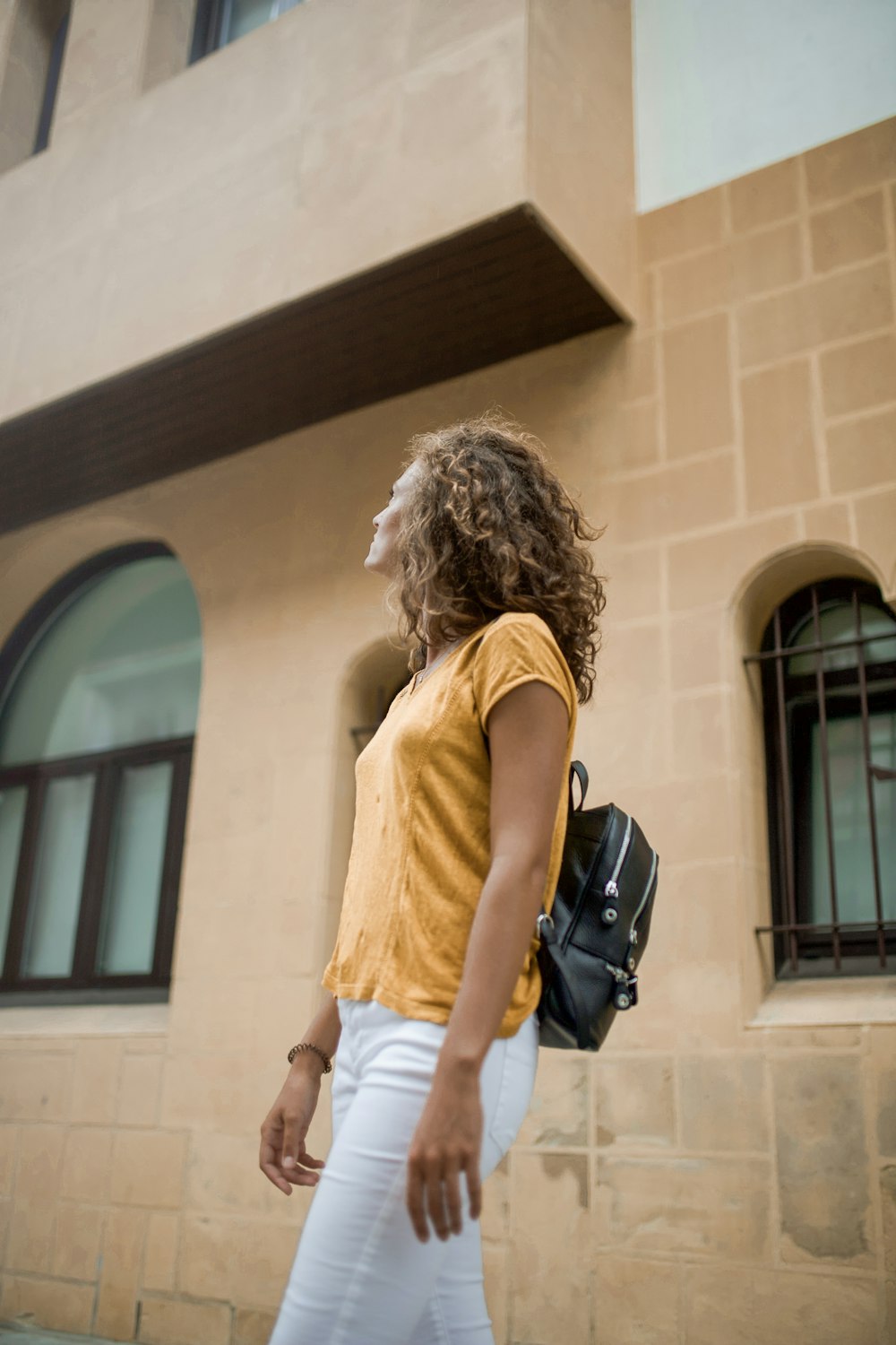 woman in yellow tank top and white shorts carrying black backpack