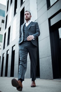 A stylish man wearing a gray suit while walking in an urban setting.