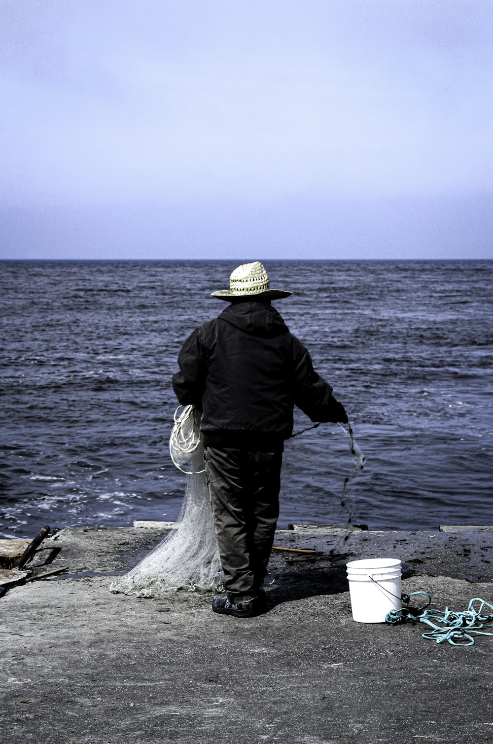 man in black jacket and brown hat holding stick near body of water during daytime