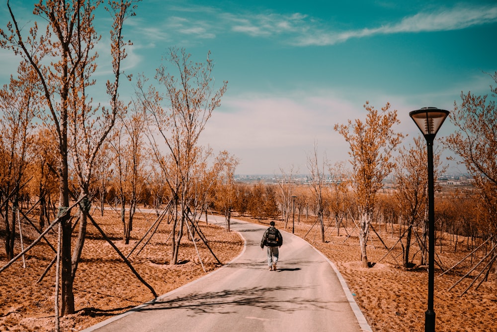 person in black jacket and black pants walking on gray concrete road during daytime