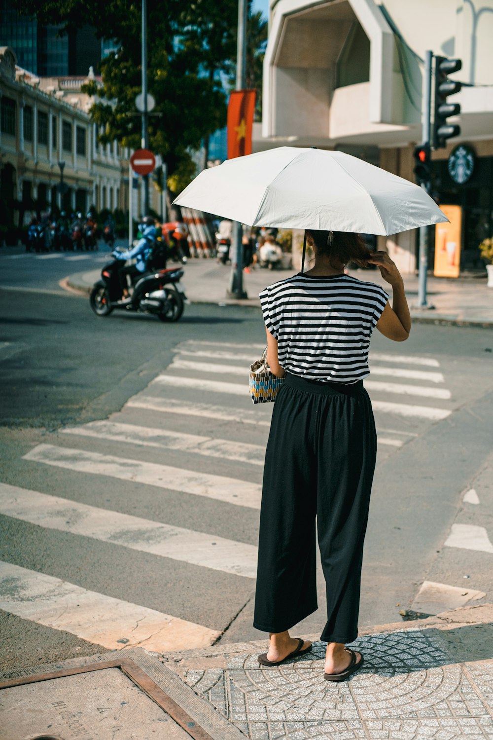 woman in black and white stripe shirt and black skirt holding umbrella walking on pedestrian lane
