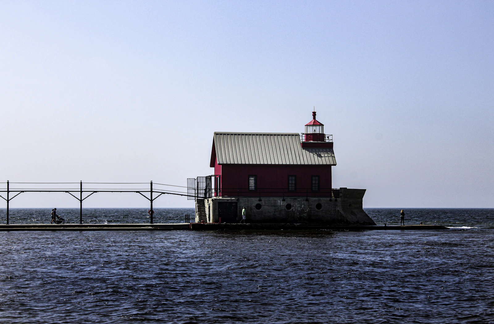 A red lighthouse at the end of a breakwater on a Great Lake.