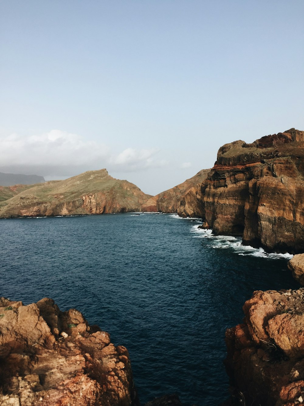 brown rocky mountain beside blue sea under blue sky during daytime