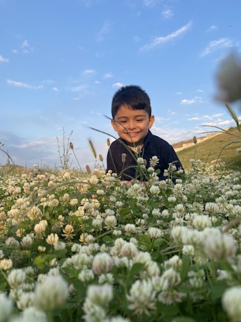 Portrait of a smiling child playing in a field of wildflowers under a bright blue sky.