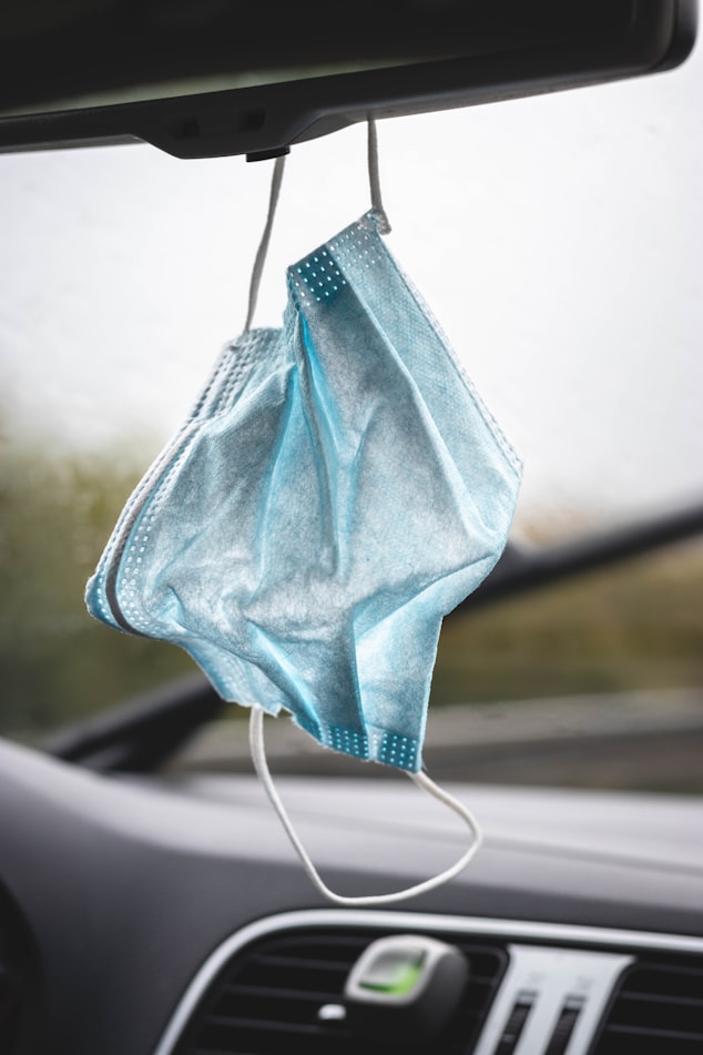 Mask dangling from rear view mirror as an employee commutes to work. Workplace reintegration means wearing masks in most cases.