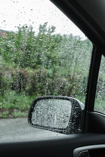 A close-up of raindrops on a car window during a gentle monsoon drive through Kerala’s countryside.