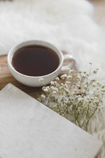 tasse en céramique blanche remplie de thé sur un plateau en bois avec de petites fleurs à côté