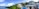 A panoramic view of a luxurious resort featuring vibrant tropical greenery surrounding a curved swimming pool. Multiple villas with large windows and balconies are situated on a lush hill. The sky is partly cloudy and the calm ocean can be seen on the left.