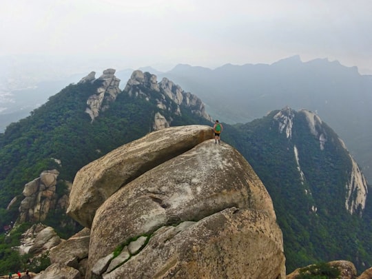 person in black jacket standing on gray rock mountain during daytime in Bukhansan South Korea