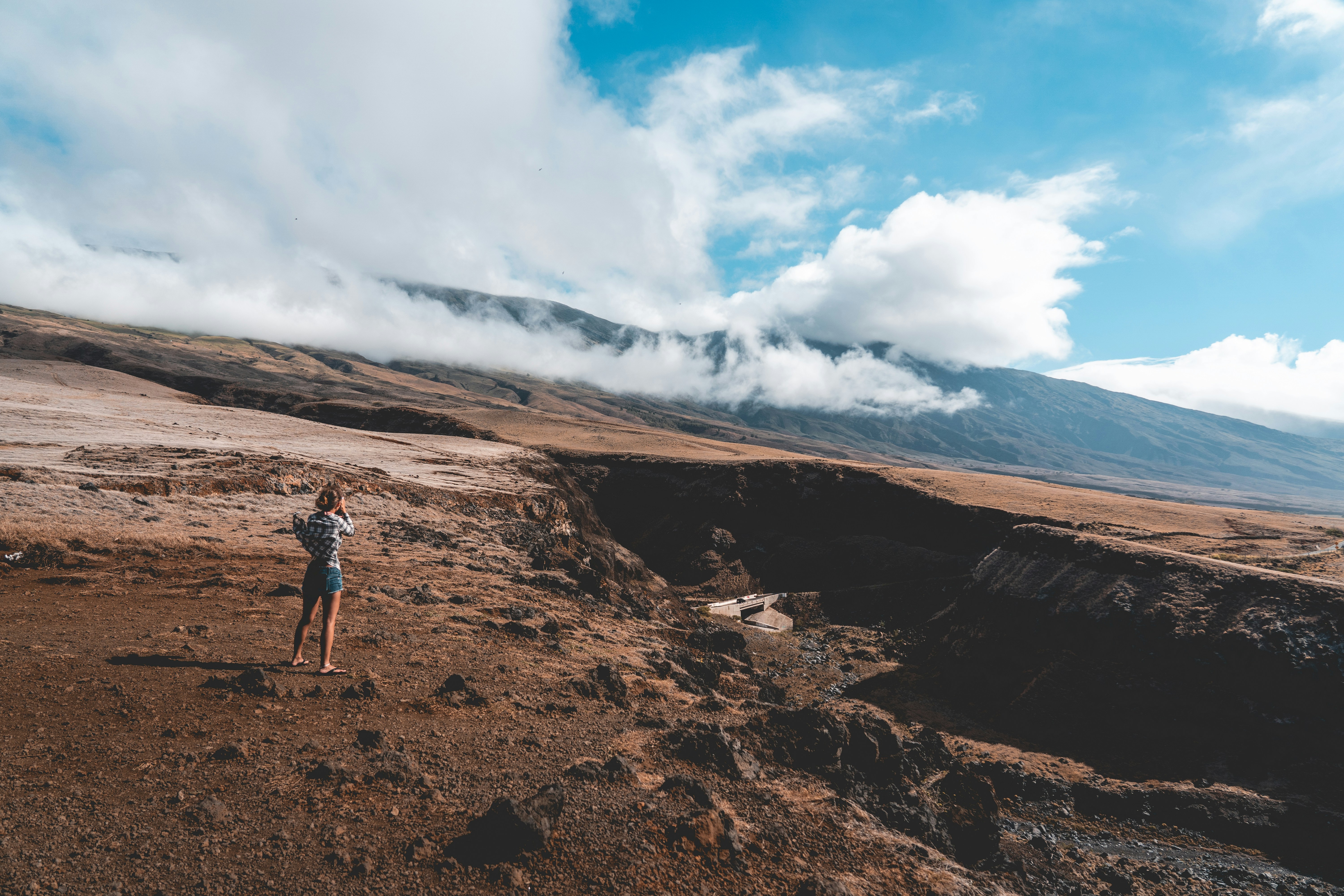 man in black jacket standing on brown rock formation under white clouds and blue sky during