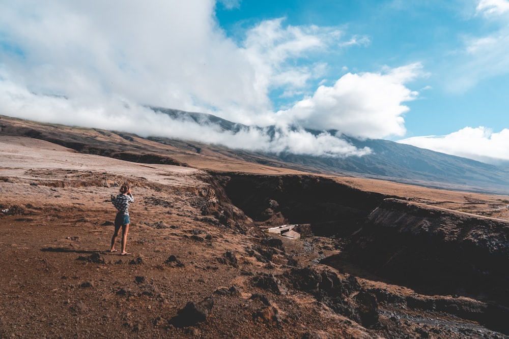 homme en veste noire debout sur la formation rocheuse brune sous les nuages blancs et le ciel bleu pendant