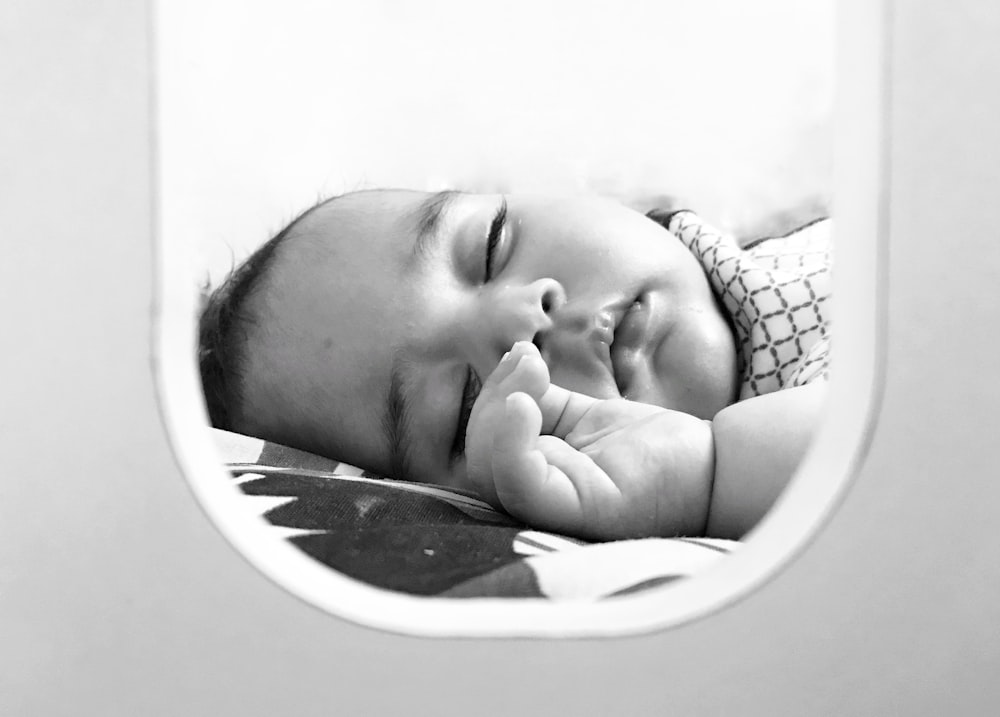 grayscale photo of baby lying on bed
