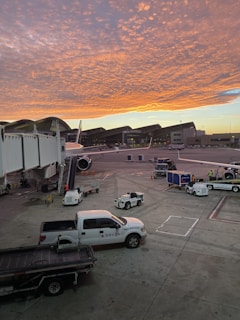 Ground support vehicles lined up next to an airplane on the tarmac at sunset