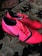 A pair of bright red athletic shoes with black accents and laces are placed on a patterned carpet. The shoes have a sleek, modern design with textured detailing and branding visible on the sides.