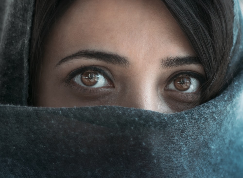 Frau mit blauen Augen, die ihr Gesicht mit blauem Textil bedecken