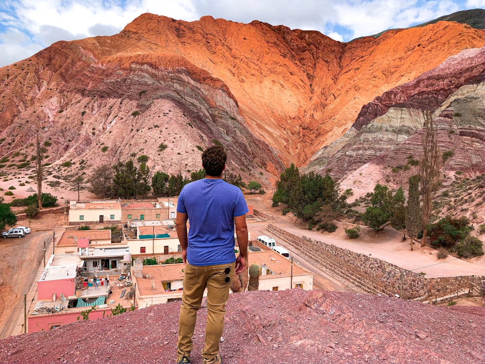 man in blue shirt and brown pants standing near brown rock formation during daytime