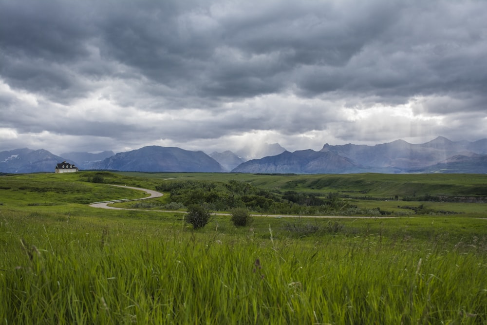 green grass field near mountain under cloudy sky during daytime