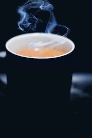 A close-up of a steaming cup of dark, aromatic instant coffee set against a deep green background with gold accents.