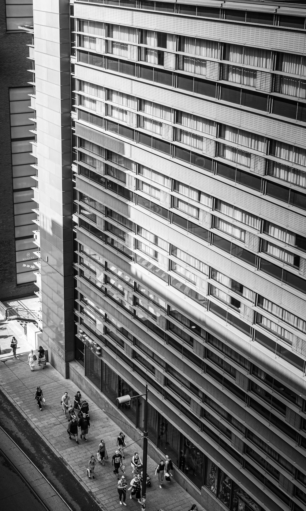 grayscale photo of people walking on street in between high rise buildings