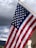 An American flag is waving against a backdrop of dark and cloudy skies. The flag's stripes and stars are prominently displayed, capturing a sense of movement and patriotism.