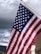An American flag is waving against a backdrop of dark and cloudy skies. The flag's stripes and stars are prominently displayed, capturing a sense of movement and patriotism.