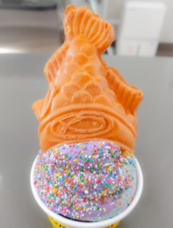 A kawaii Japanese-style ice cream cone shaped like a taiyaki fish, with soft yogurt ice cream and a playful panda mascot licking the cone.