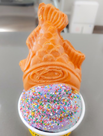 A kawaii Japanese-style ice cream cone shaped like a taiyaki fish, with soft yogurt ice cream and a playful panda mascot licking the cone.