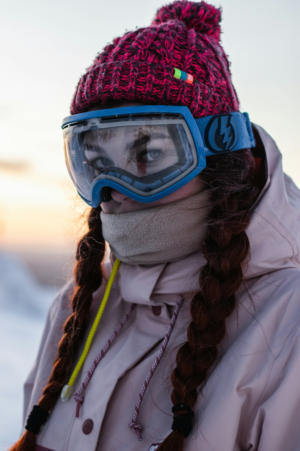 woman in white jacket wearing blue goggles and red knit cap