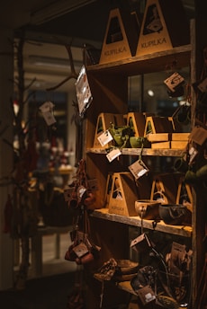A wooden shelf in a store displays various handcrafted items such as cups, bowls, and utensils packaged in eco-friendly cardboard boxes. These items hang from hooks, showcasing earthy tones and rustic designs, with natural lighting emphasizing the warm atmosphere.