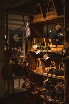 A wooden shelf in a store displays various handcrafted items such as cups, bowls, and utensils packaged in eco-friendly cardboard boxes. These items hang from hooks, showcasing earthy tones and rustic designs, with natural lighting emphasizing the warm atmosphere.