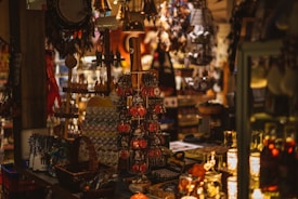 A warmly lit shop interior with a variety of souvenirs on display, including keychains, baskets, and other trinkets. The atmosphere is cluttered but cozy, filled with hanging decorations and shelves packed with items.