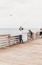 man and woman holding fishing rods standing on wooden dock during daytime