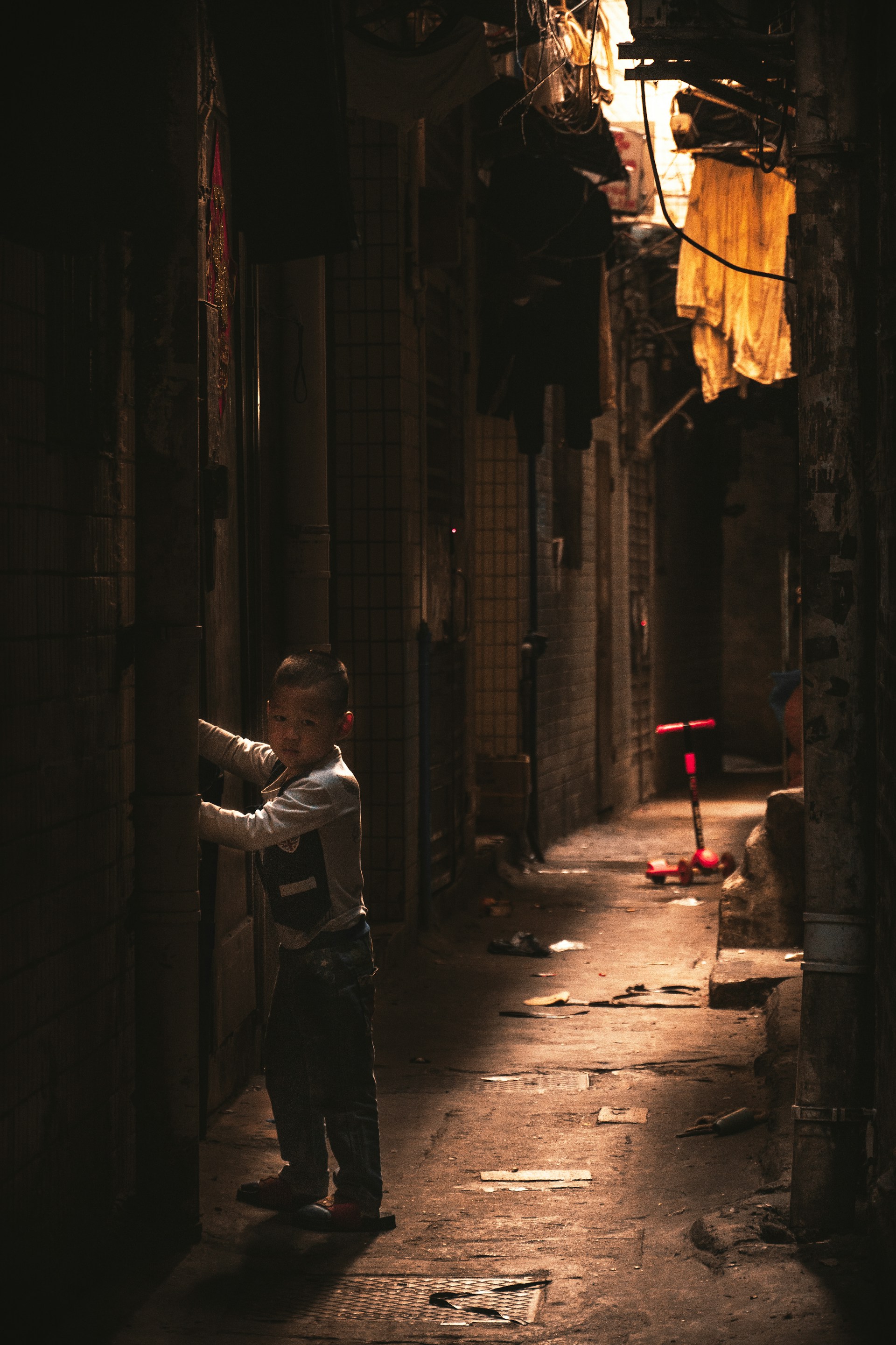 A child playing near a dusty alley, framed by peeling walls that whisper tales of a forgotten neighborhood.