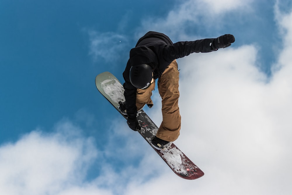 man in black jacket and brown pants riding white and red snowboard