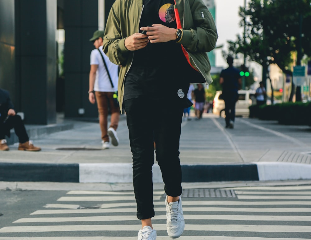 man in green jacket and black pants walking on pedestrian lane during daytime