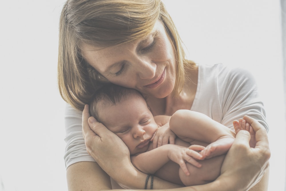 Frau im weißen T-Shirt mit Rundhalsausschnitt trägt Baby