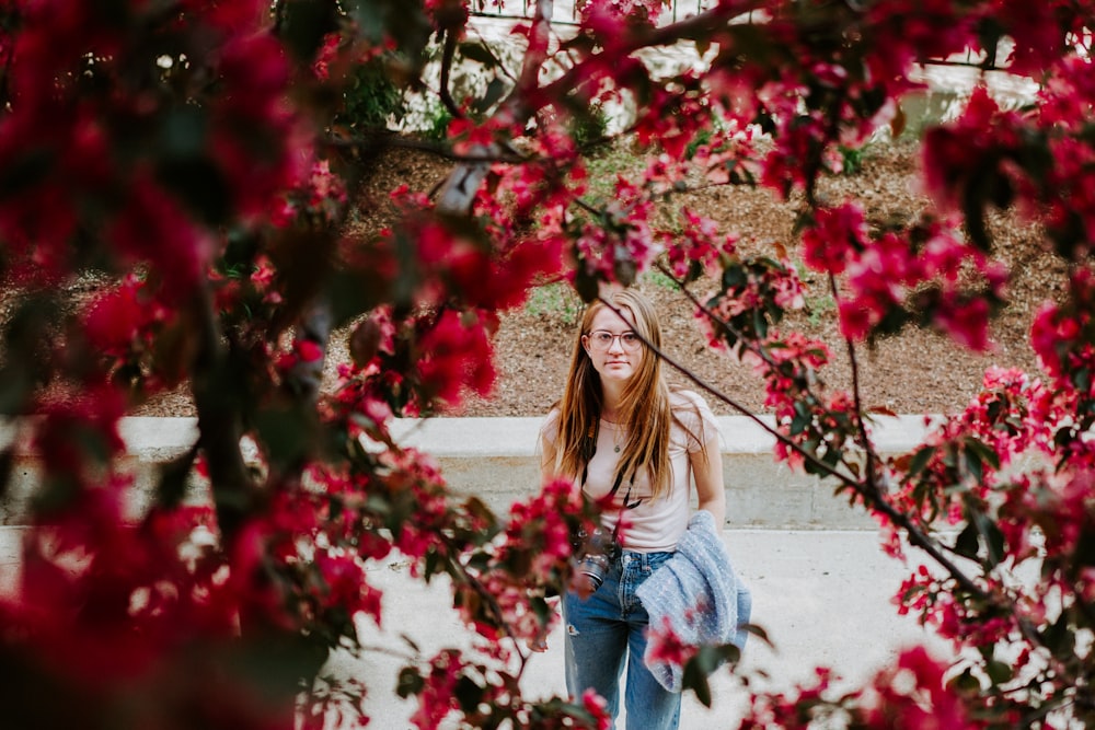 woman in white long sleeve shirt and blue denim jeans standing near red flowers