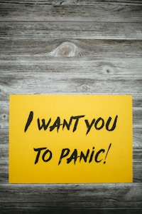 A yellow paper with bold black text stating 'I want you to panic!' is placed on a rustic wooden surface with a grayish-brown weathered texture.