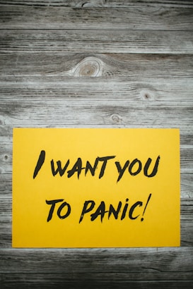 A yellow paper with bold black text stating 'I want you to panic!' is placed on a rustic wooden surface with a grayish-brown weathered texture.