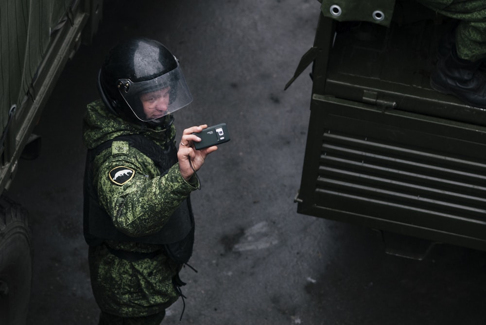 man in green and black camouflage jacket holding black smartphone