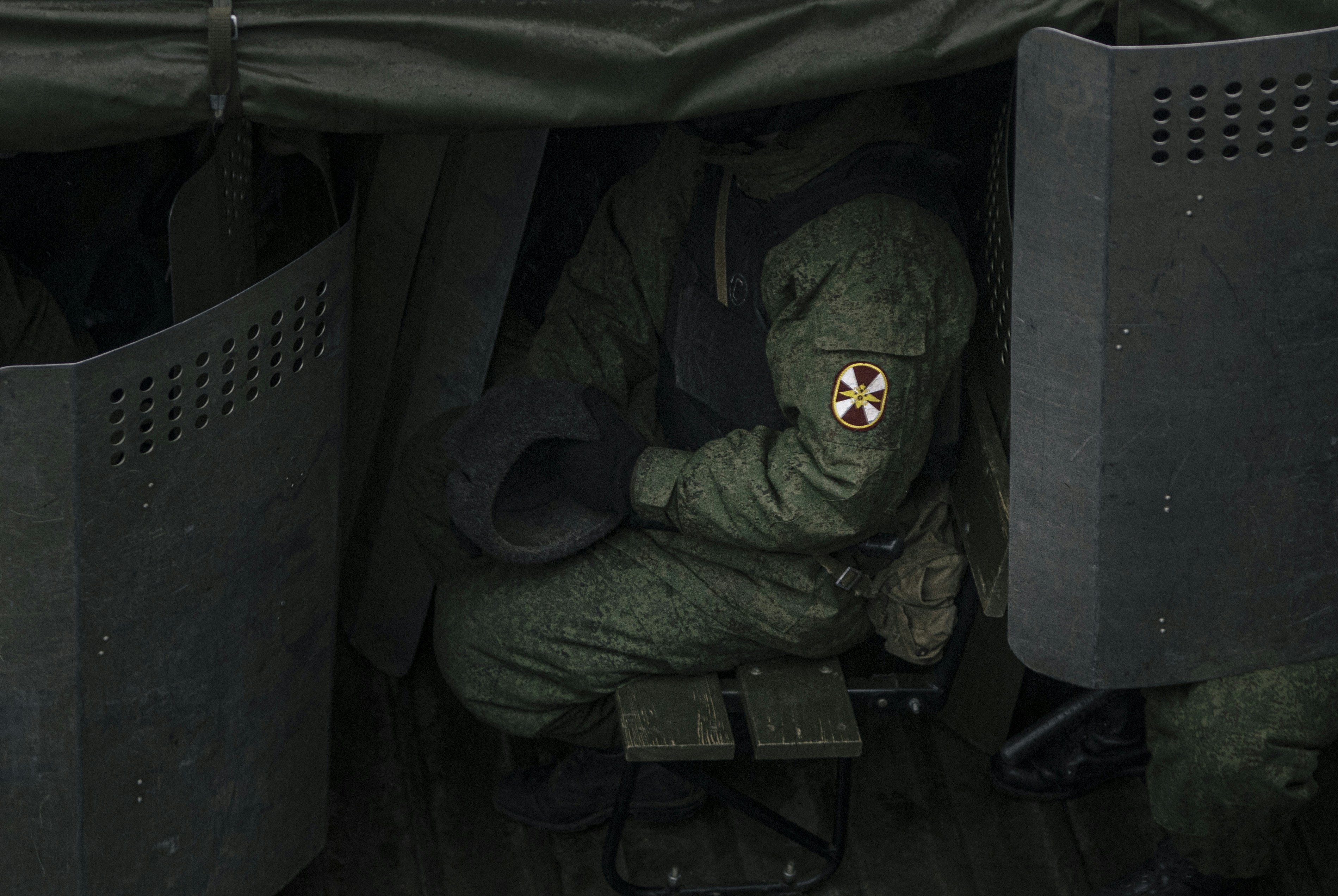 A military man in equipment in the back of a military truck.