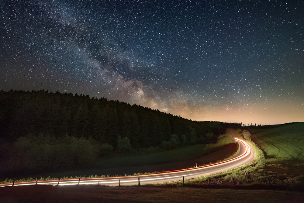 gray concrete road between green trees under blue sky during night time