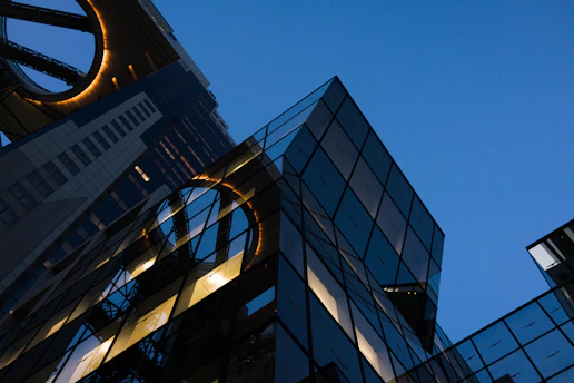 A sleek architectural close-up of a modern glass building reflecting a deep navy sky at dusk.