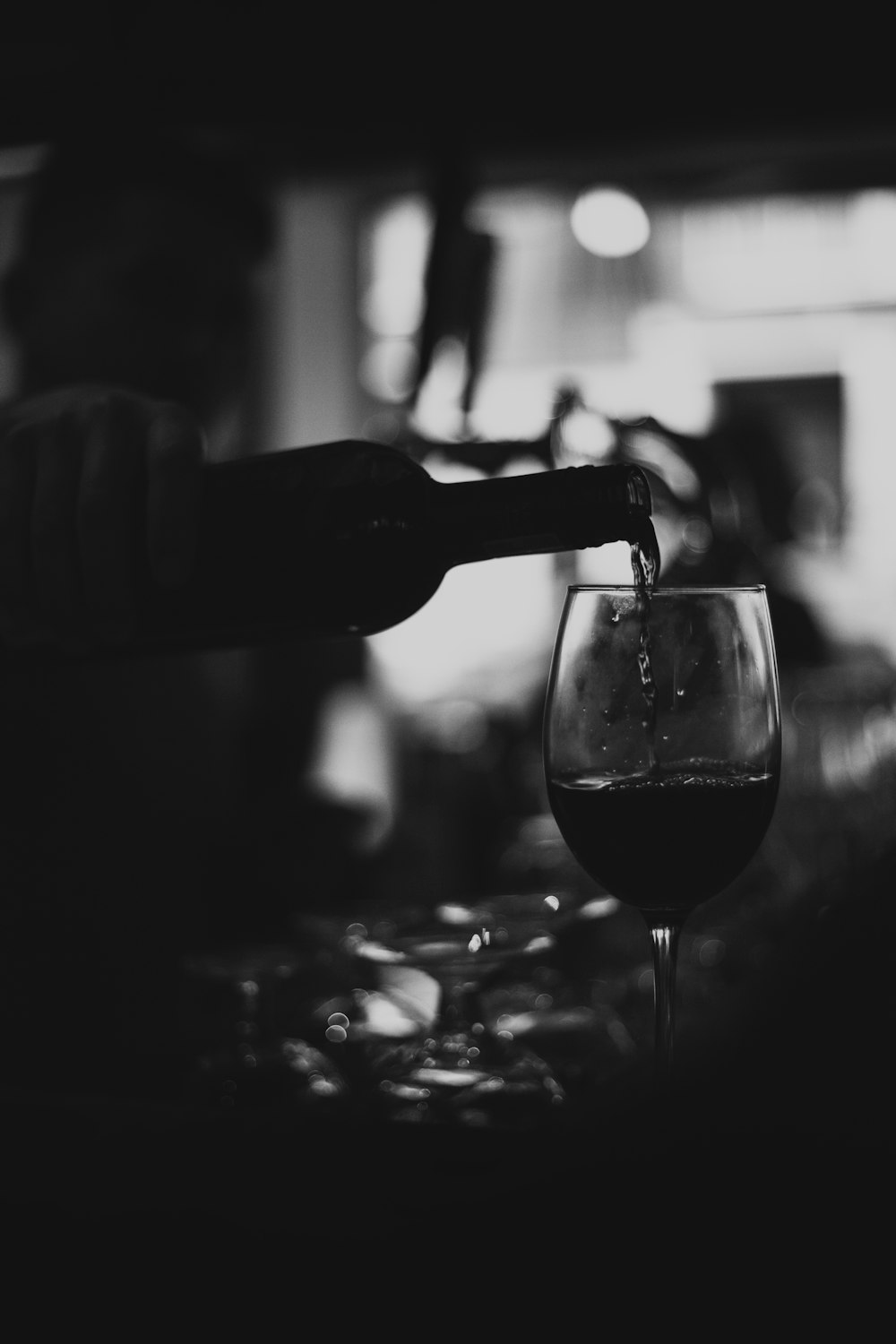 Foto en escala de grises de una persona que vierte vino en una copa de vino transparente