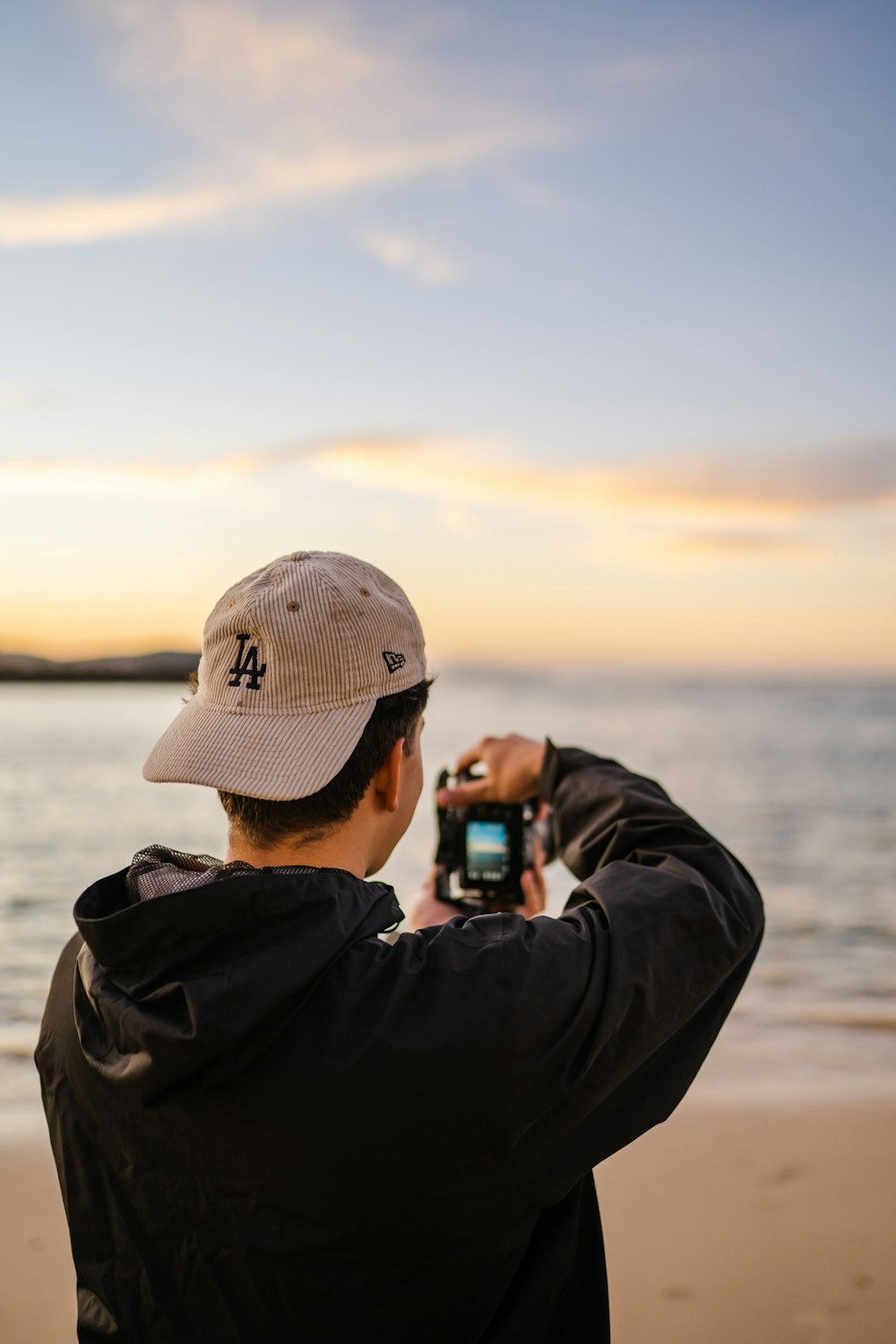 man in gray jacket and gray cap taking photo of sea during daytime